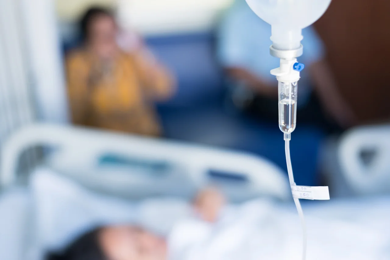 IV infusion drip with a reclining patient and companion softly blurred in the background